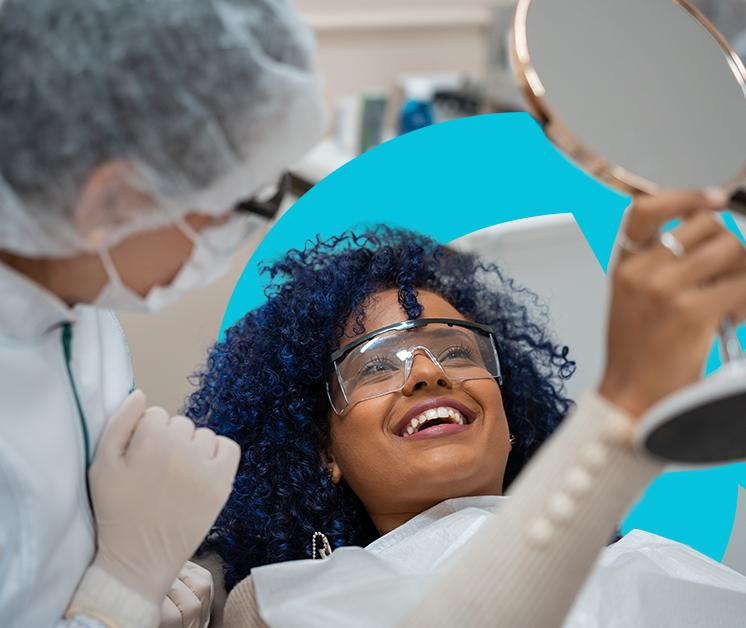 Mujer en un consultorio de Odontología observando con un espejo como quedo su sonrisa 